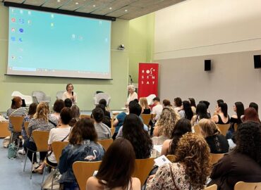 Visió des de darrera de les persones assistens a la jornada i, al fons, la ponent amb el micro a la mà.