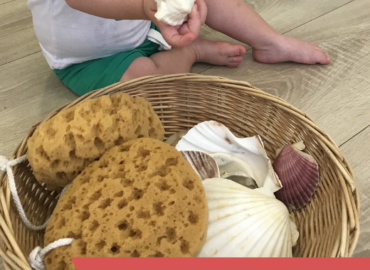 Infant manipulant un cargol de mar i una panera dels tresors amb elements del mar